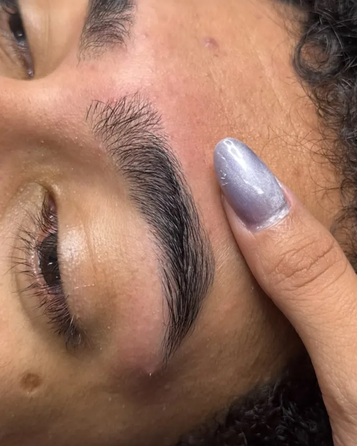 Sobrancelha recém-feita, com a mão da profissional ao lado